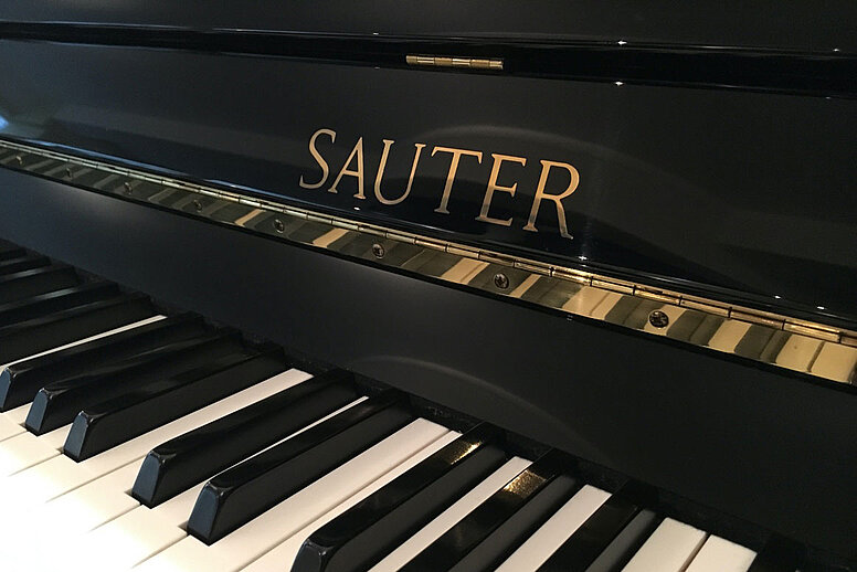 Ein schwarzes Klavier im Bildausschnitt. Man erkennt nur einige wenige weiße und schwarze Tasten.