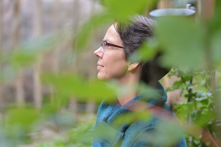 Eine weibliche Person mit einer Brille auf der Nase, richtet ihren Blick nach links und schaut in die Ferne.